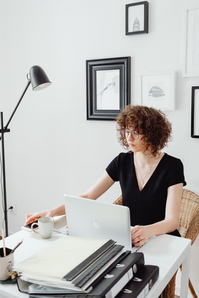 Woman with curly hair working on a laptop in a stylish modern office with artwork on the walls.